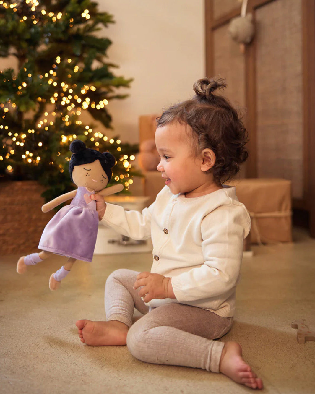 Kind speelt met Doll Daisy voor een verlichte kerstboom